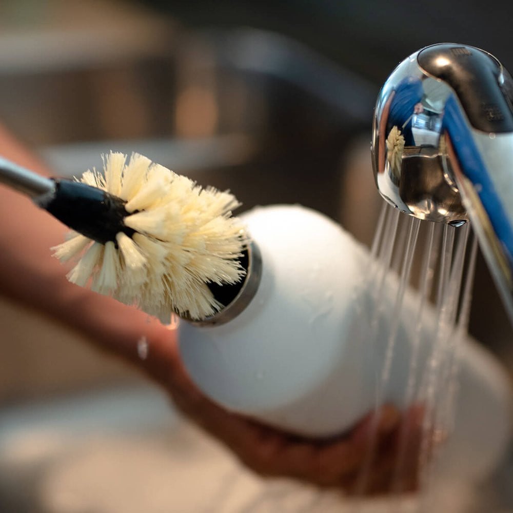 Escova para Higienização de Garrafas e Copos - Kouda em uso durante a limpeza de uma garrafa sob água corrente.