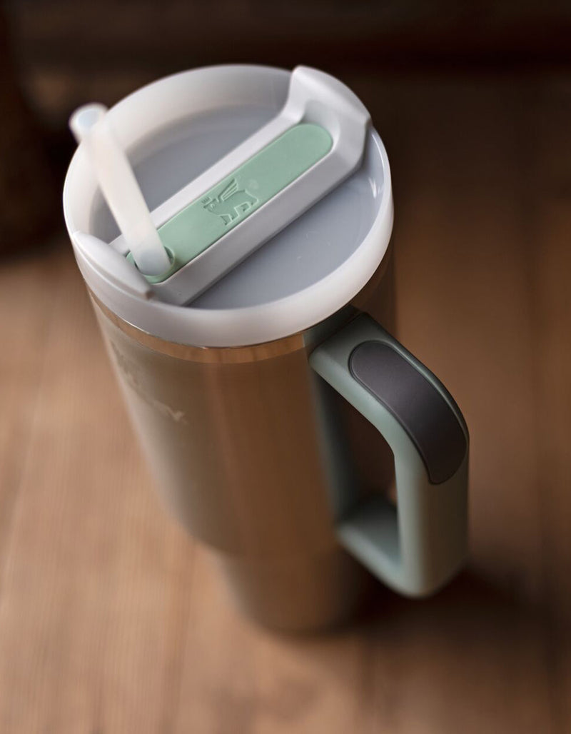 Copo Quencher Stanley 887ml com alça ergonômica e tampa de 3 posições, vista de cima, design moderno sobre mesa de madeira.