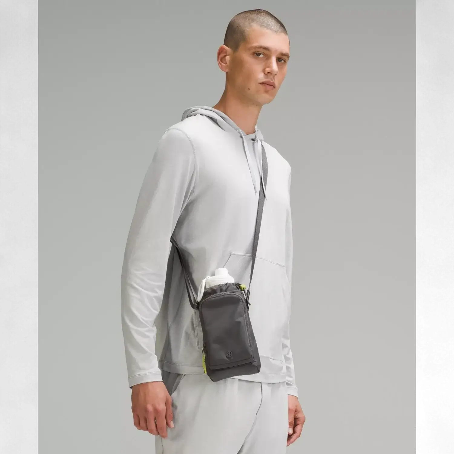 Homem usando a Bolsa para Garrafa Térmica - Cross Bottle Lululemon na cor cinza claro com garrafa branca