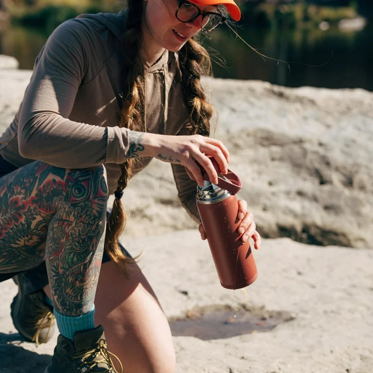 Garrafa Térmica Camelbak Thrive 740ml sendo usada ao ar livre, ideal para manter a hidratação durante atividades.