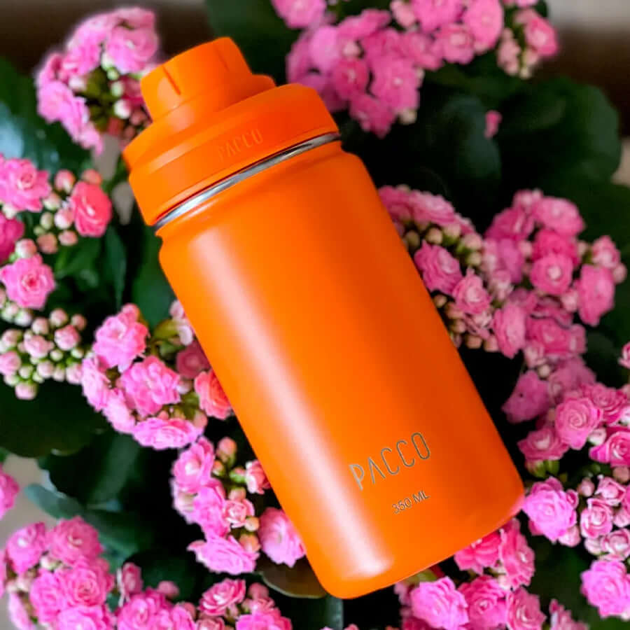 Garrafa Térmica PACCO Hydrav2 350ml laranja entre flores, mantendo bebidas frias por 24h e quentes por 12h.