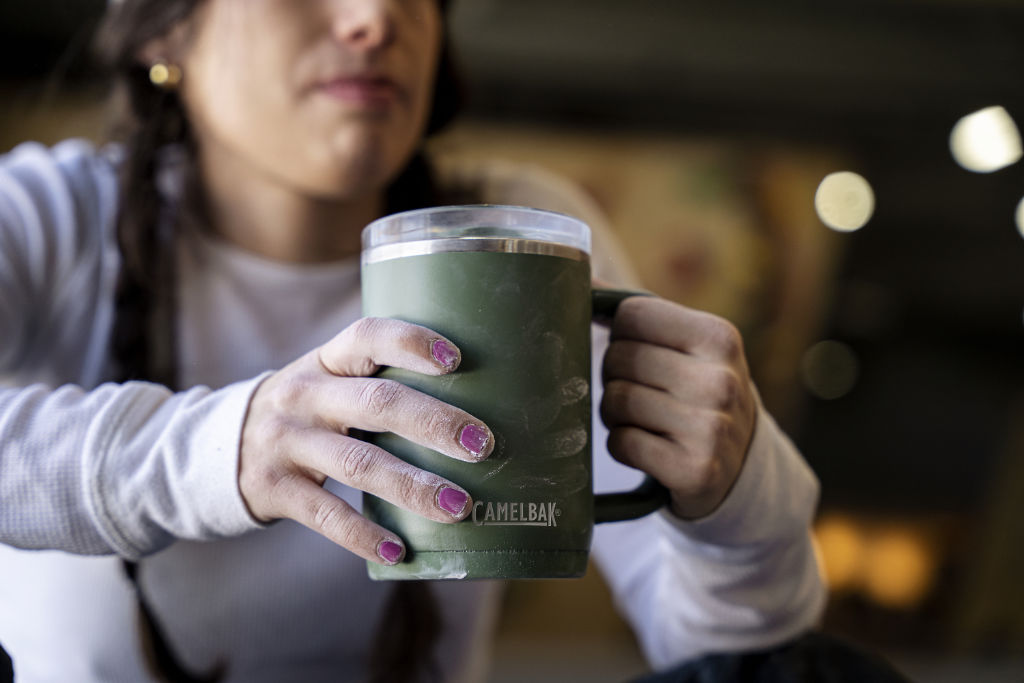 Mulher segurando uma Caneca Térmica Thrive Camelbak 470ml verde em ambiente urbano