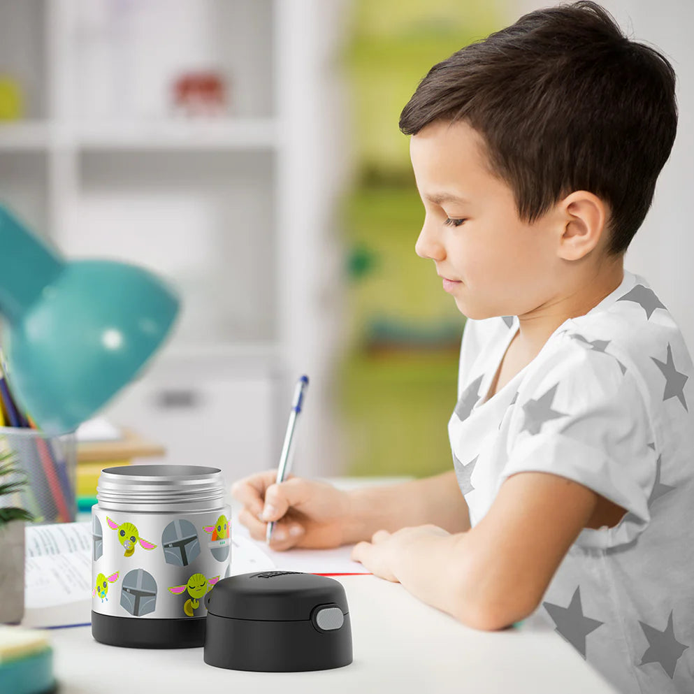 Criança escrevendo ao lado de um Pote Térmico Thermos ® 283g Funtainer aberto com estampa divertida.