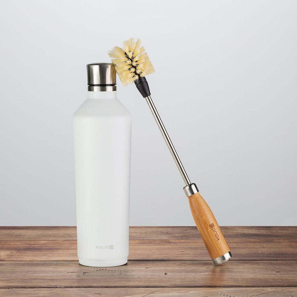 Escova para Higienização de Garrafas e Copos - Kouda ao lado de uma garrafa branca sobre uma mesa de madeira.