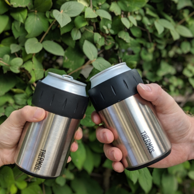 Mãos segurando Porta Lata Térmico Munique Prata Thermos - 355ml com fundo de vegetação.