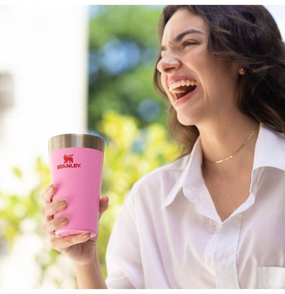 Mulher sorrindo segurando Copo Térmico de Cerveja Stanley - 473ml rosa, ideal para manter bebidas geladas por até 4 horas.