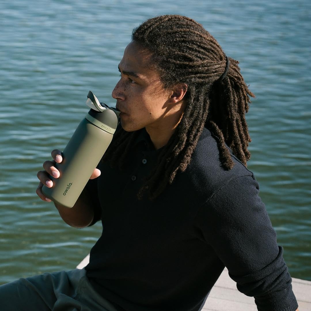 Pessoa bebendo de uma Garrafa Térmica Owala FreeSip - 946ml | 32oz com design moderno à beira de um lago.
