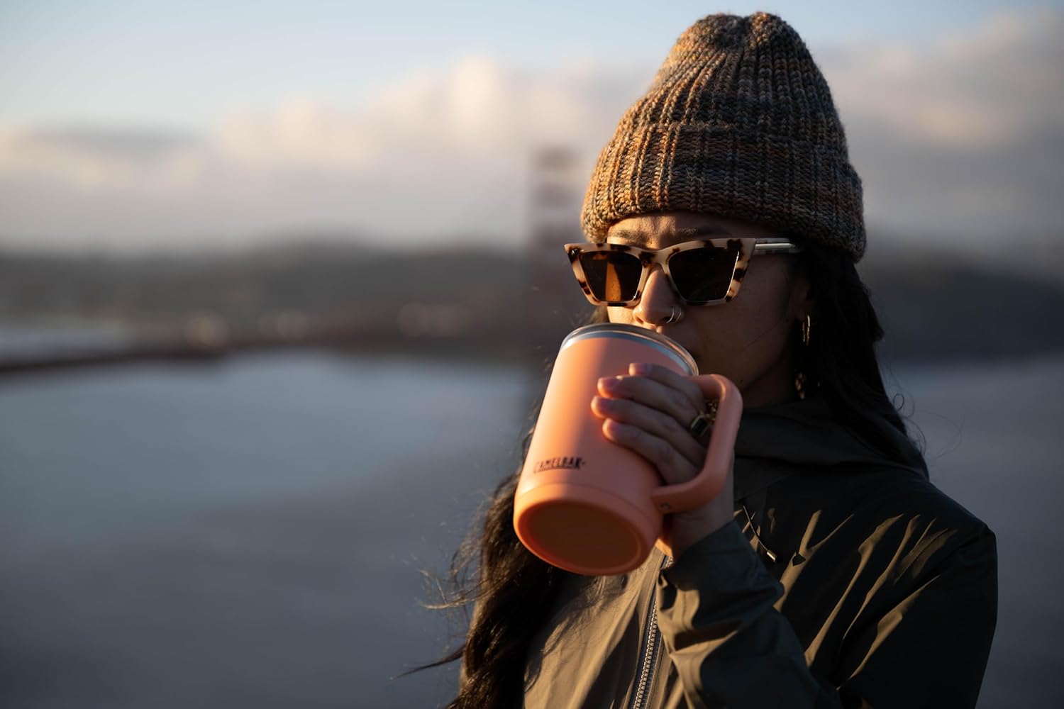 Mulher bebendo de uma Caneca Térmica Thrive Camelbak 470ml laranja ao ar livre