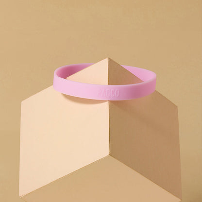 Anel de Silicone PACCO rosa com design ergonômico, oferecendo conforto e aderência para garrafas, sobre fundo geométrico.