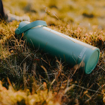 Garrafa Térmica Thrive Camelbak 1,18L repousando sobre a grama em uma paisagem natural.