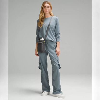 Mulher com Bolsa para Garrafa Térmica - Cross Bottle Lululemon, vestindo calça e blusa cinza, destacando estilo e funcionalidade.