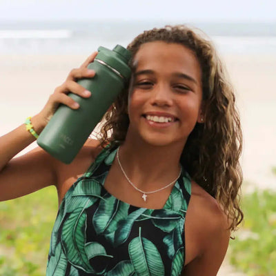 Jovem segurando Garrafa Térmica PACCO Hydrav2 500ml verde em uma praia, destacando o design elegante e eficiência térmica.