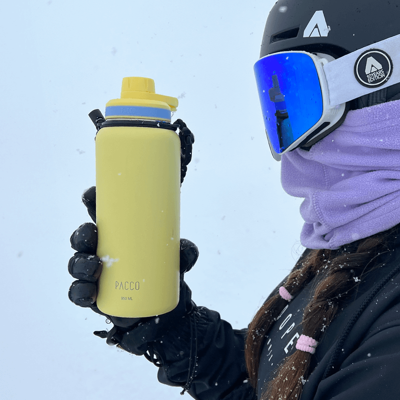 Pessoa segurando Garrafa Térmica PACCO Hydrav2 950ml amarela em ambiente de neve, destacando o design moderno e conforto térmico.