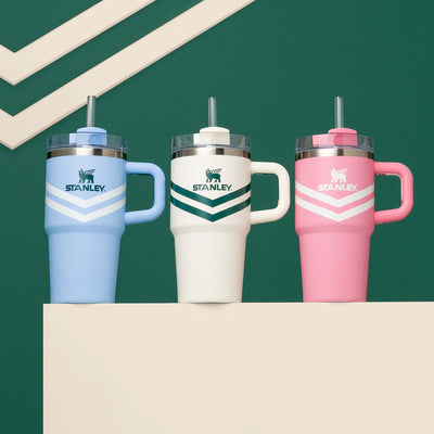 Copo Quencher Stanley | 591ml em azul, branco e rosa sobre fundo verde.
