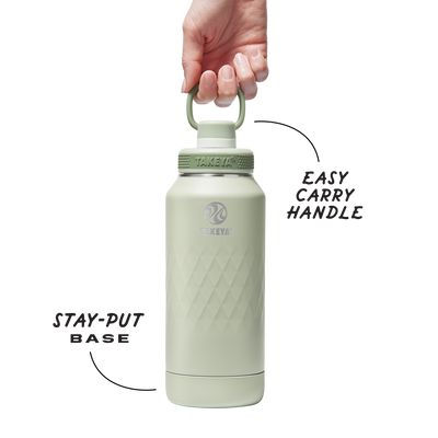 Mão segurando Garrafa Térmica Takeya 950ml Spout Lid Sport com design verde elegante e tampa prática para esportes.