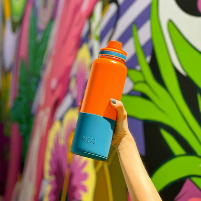 Garrafa Térmica PACCO Hydrav2 1200ml sendo segurada em frente a um mural colorido, destacando design e tecnologia.