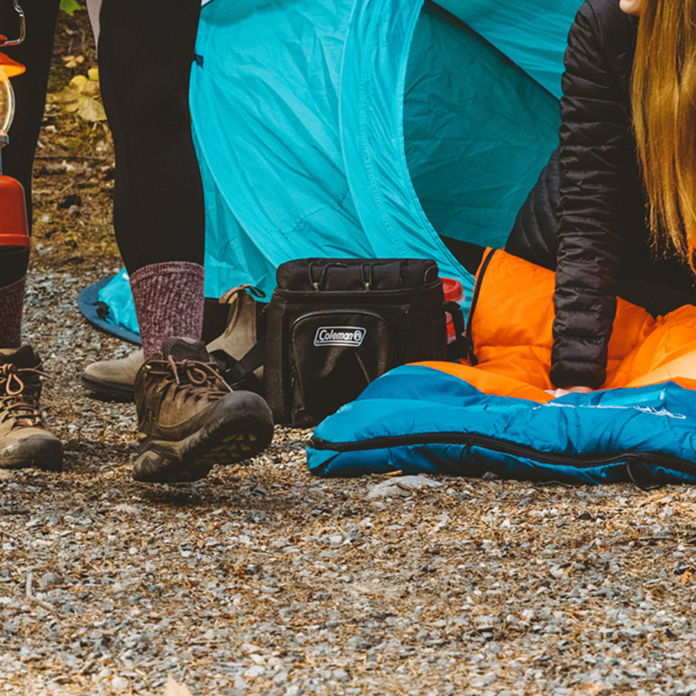 Bolsa Térmica Chiller™ 16 Latas Coleman em acampamento, perto de barraca azul, mostra praticidade e estilo outdoor.