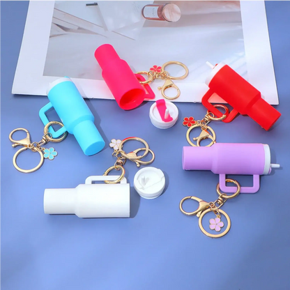 Chaveiro Copo Stanley Quencher em cores diferentes exibidos em um fundo azul com chaveiros de flores.