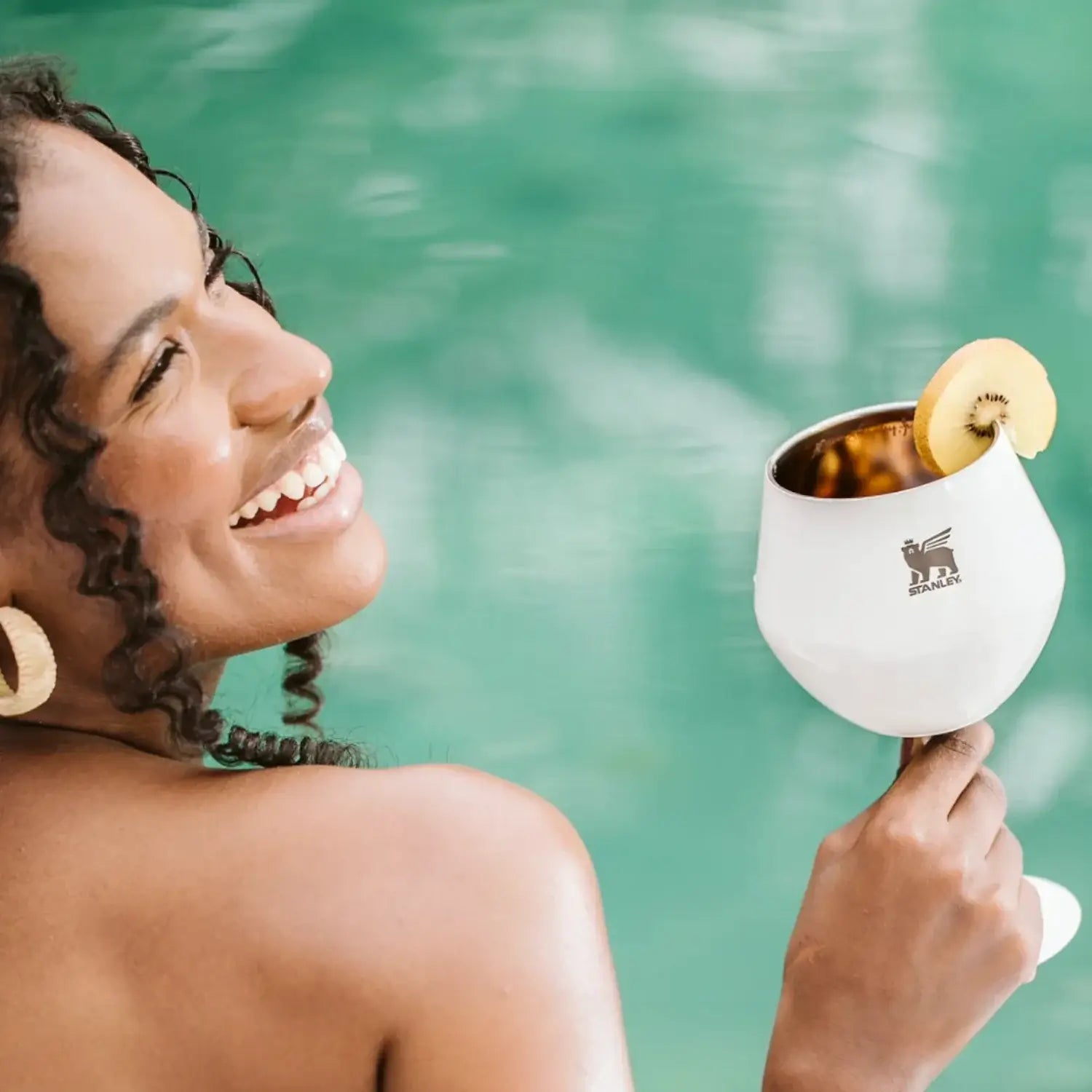 Mulher sorridente segurando Taça Térmica Cocktail Glass Stanley 414ml com kiwi, ao lado de piscina.