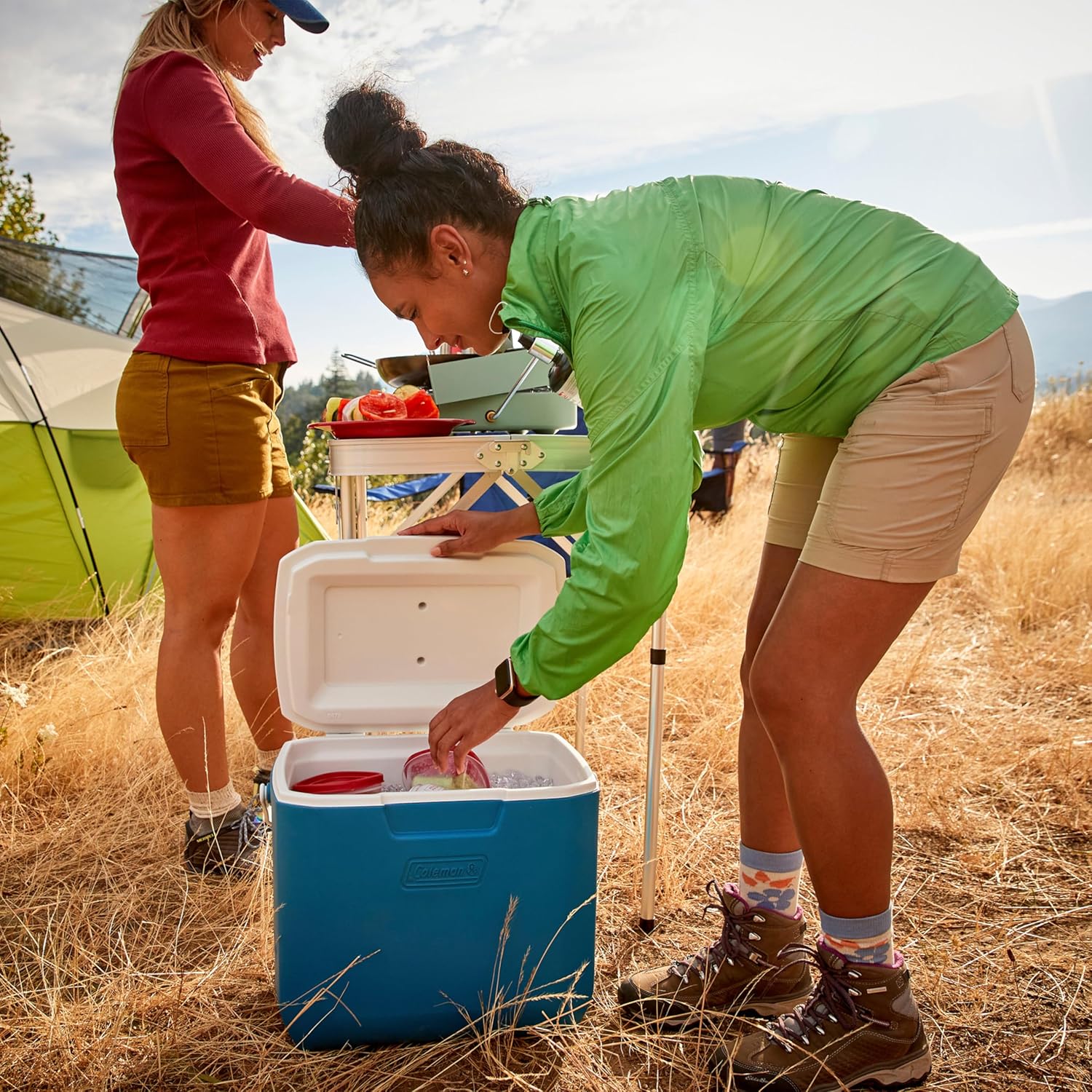 Mulher usando Coleman Chiller Cooler 30QT em acampamento, ideal para manter alimentos e bebidas gelados com isolamento térmico TempLock™.