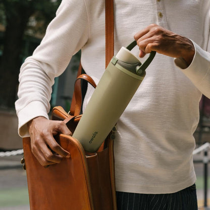Pessoa colocando Garrafa Térmica Owala FreeSip Sway - 887ml em uma bolsa, destacando praticidade e estilo para hidratação diária.