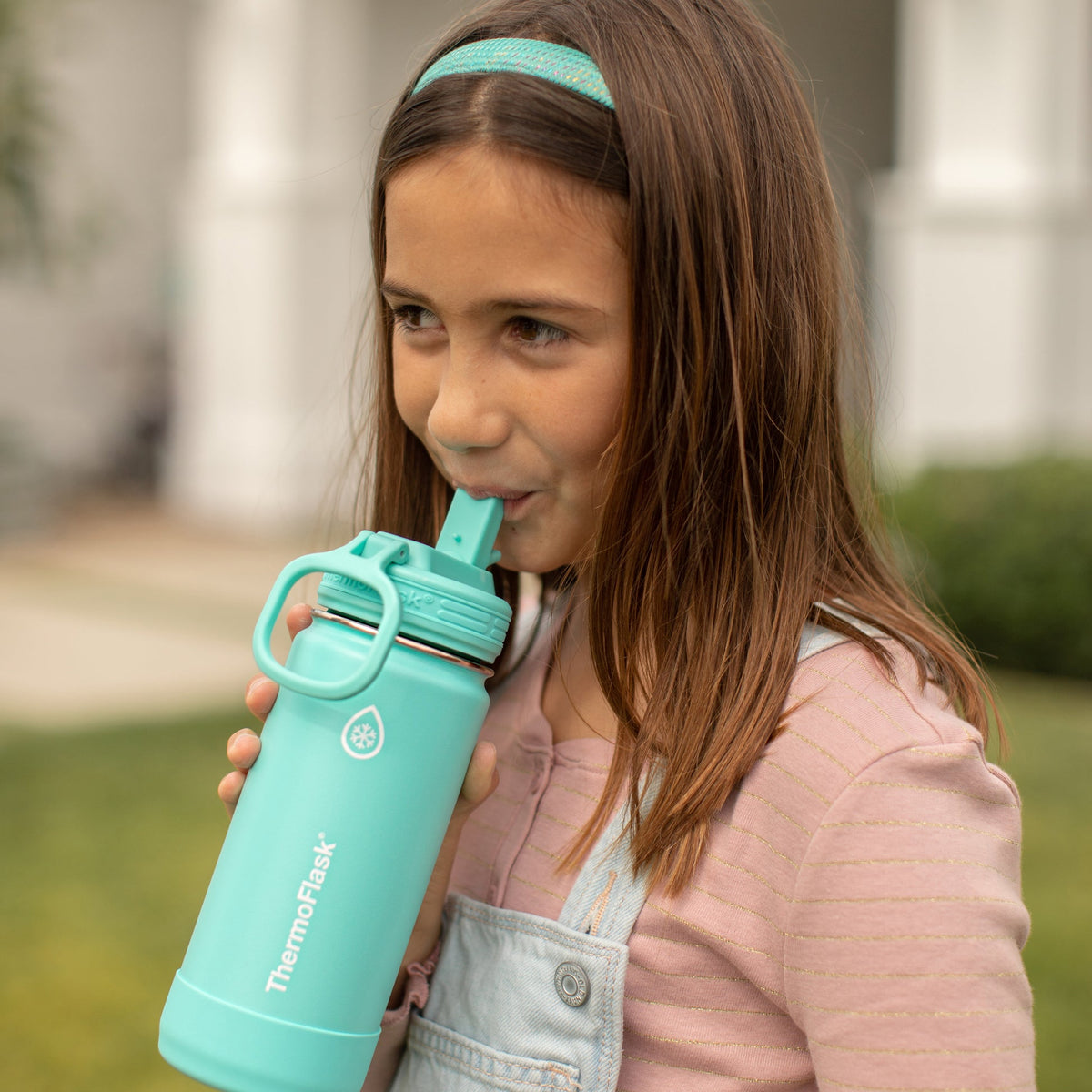 Menina bebendo de uma Garrafa Térmica Thermoflask 414ml - 16oz ao ar livre, destacando praticidade e isolamento térmico.