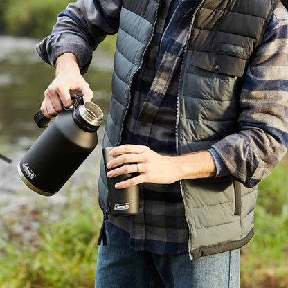 Pessoa usando o Growler 1,9L Preto Coleman ao ar livre, mantendo bebidas na temperatura ideal com isolamento a vácuo.
