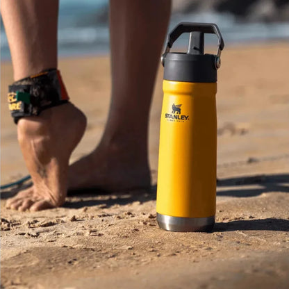 Garrafa Térmica Flip Straw Stanley 651ml amarela na praia, ideal para bebidas frias, com alça integrada para fácil transporte.