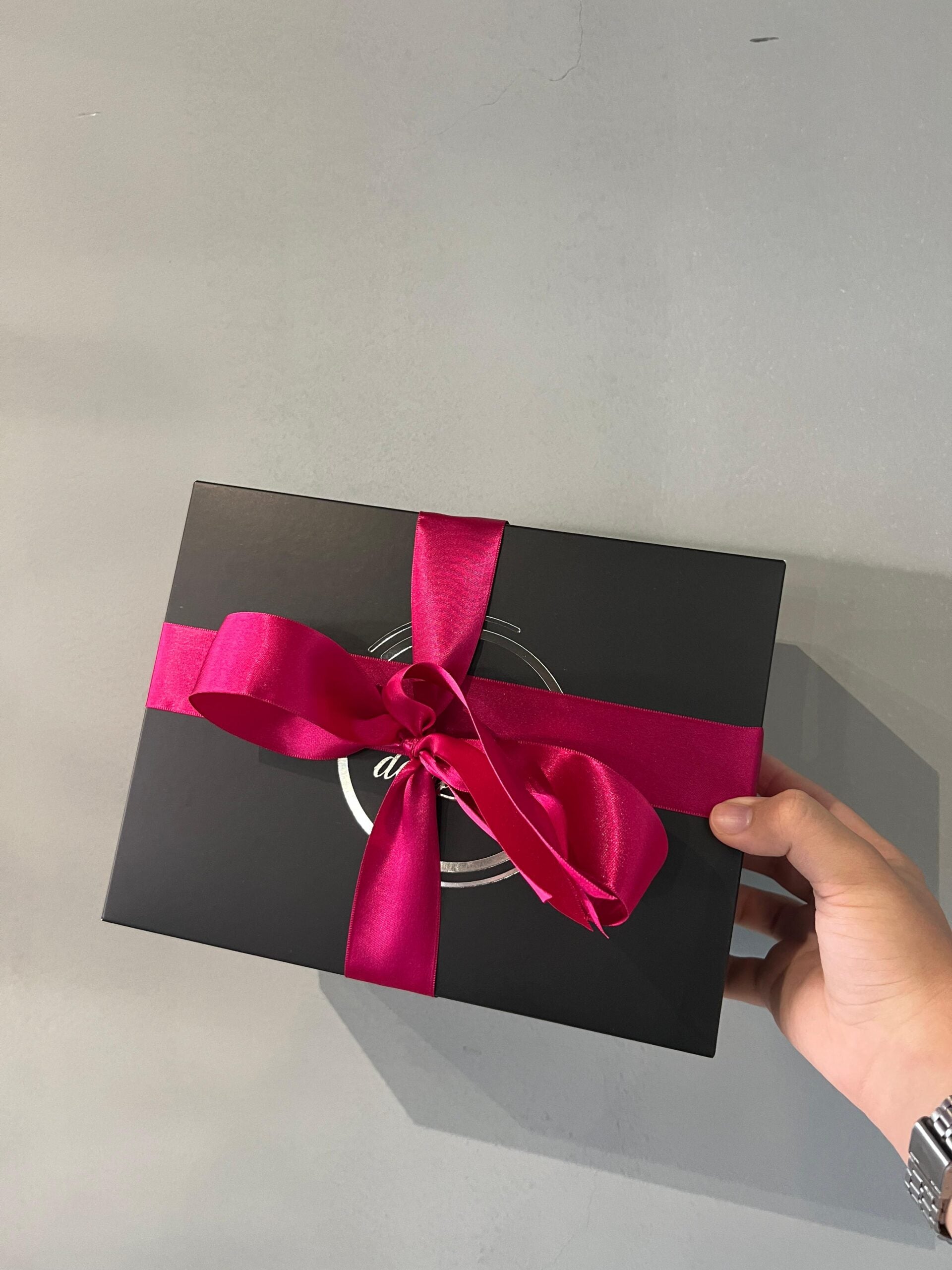 Embalagem gift wrapping elegante com laço de cetim rosa e caixa preta fosca.