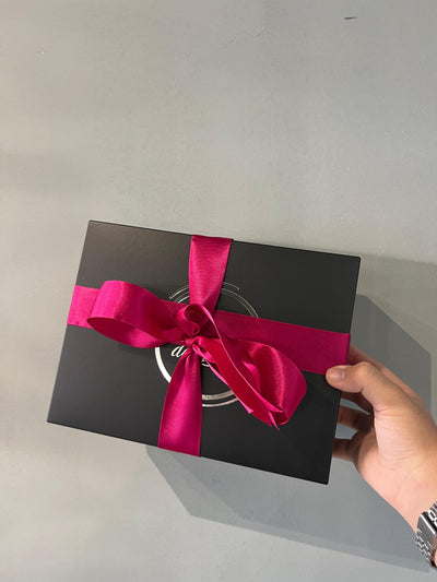 Embalagem gift wrapping elegante com laço de cetim rosa e caixa preta fosca.