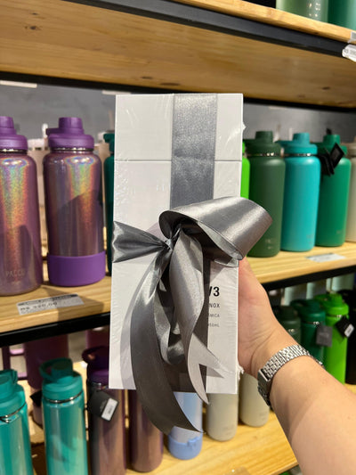 Embalagem de presentear com fita de cetim cinza, destacando o foco em gift wrapping, exibida em frente a garrafas coloridas.