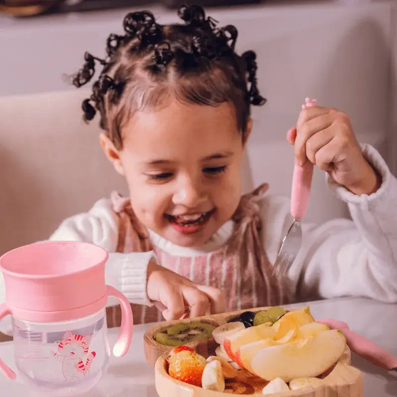 Criança usando Kit Talheres Infantil Inox e Silicone 2 Peças - Petit Piá com design rosa e azul durante refeição saudável.
