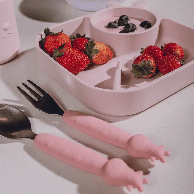 Conjunto Kit Talheres Infantil Inox e Silicone 2 Peças - Petit Piá com colher e garfo em silicone rosa, ao lado de prato infantil.