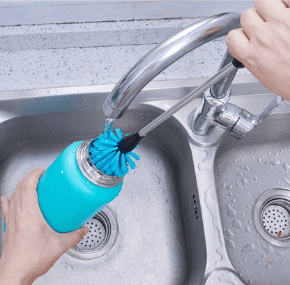 Pessoa usando Kit de Escovas para Limpeza de Garrafas, Canudos e Tampas, esfregando uma garrafa azul em uma pia, água correndo.