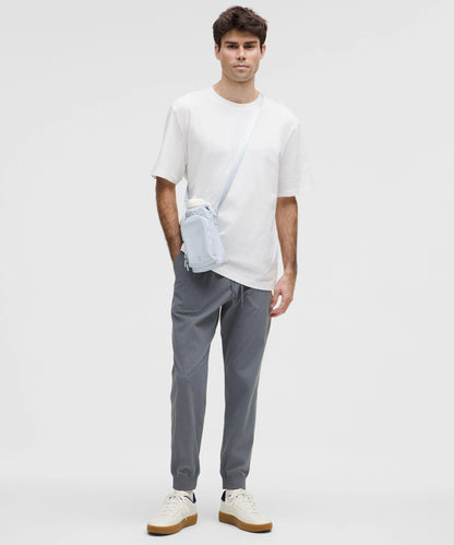 Homem usando a Bolsa para Garrafa Térmica - Cross Bottle Lululemon, estilo casual com camiseta branca e calças cinza.