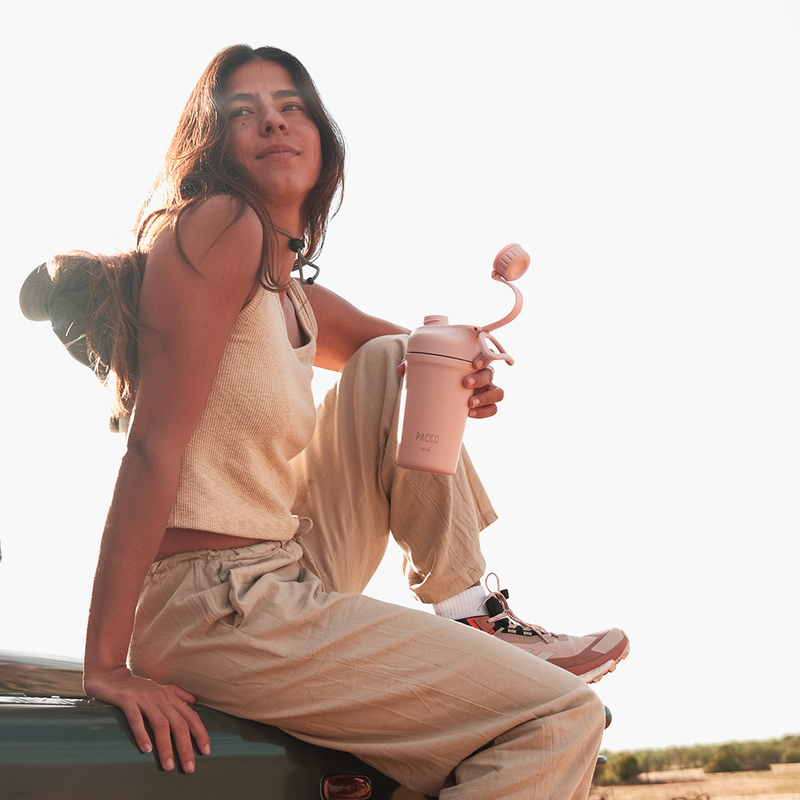 Mulher ao ar livre segurando Copo Térmico PACCO Shaker 600ml rosa, ideal para viagens e academia, com tecnologia de isolamento térmico.