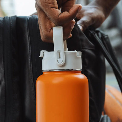 Pessoa segurando uma Tampa PACCO Duo laranja com tampa flip e canudo, ideal para hidratação versátil e fácil de transportar.