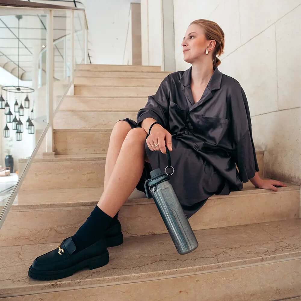 Mulher sentada segurando Garrafa Térmica Vyta 650ml PACCO | PEDRAS PRECIOSAS, design elegante e sustentável.